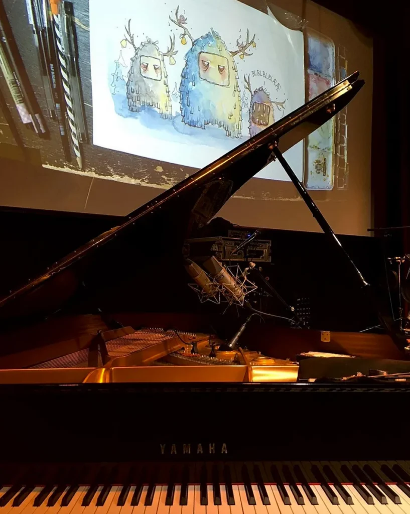A grand piano on stage at Moldejazz, with Gunvor Rasmussen’s live monster drawing projected on the big screen behind it
