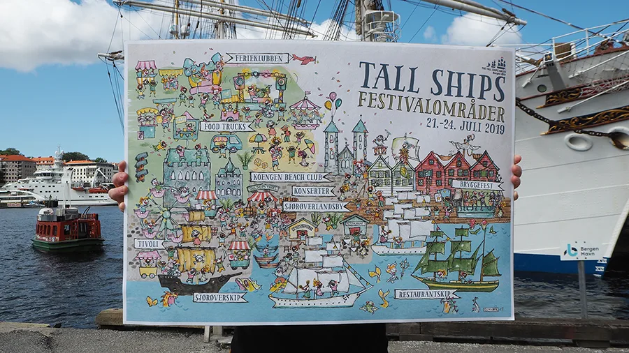 The printed Tall Ships Races festival map held up at the harbour in Bergen, with tall ships behind